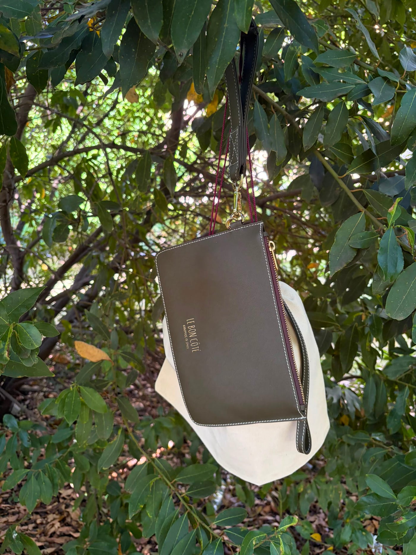 Cartera de piel verde caza con su bolsa de tela, colgada de un árbol